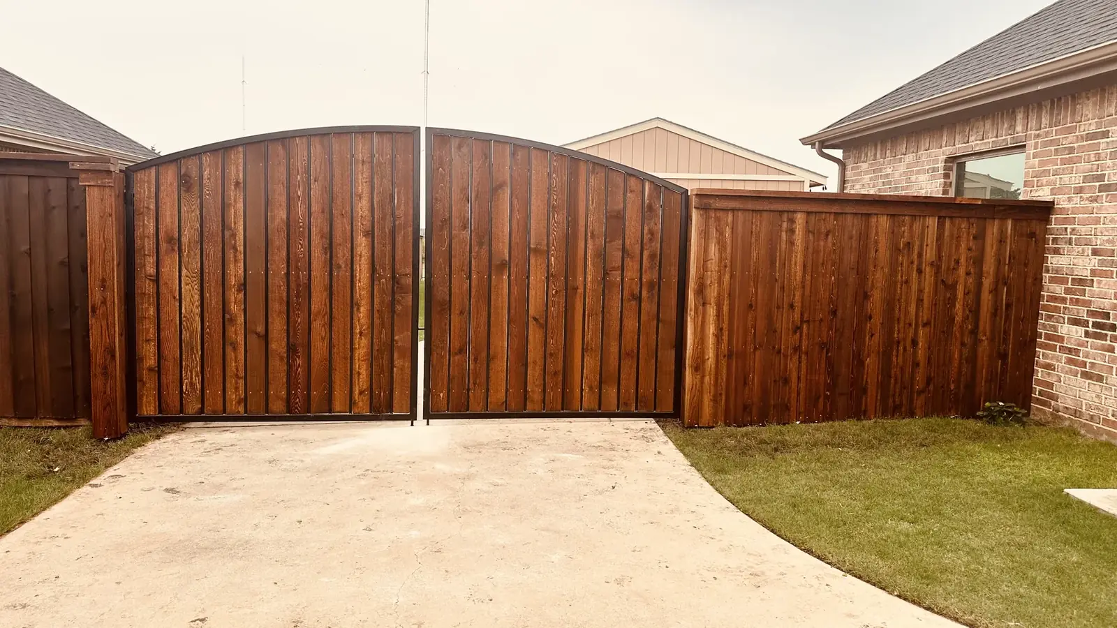 Arched cedar driveway gate in a steel frame with matching fence in Navarro County, Texas