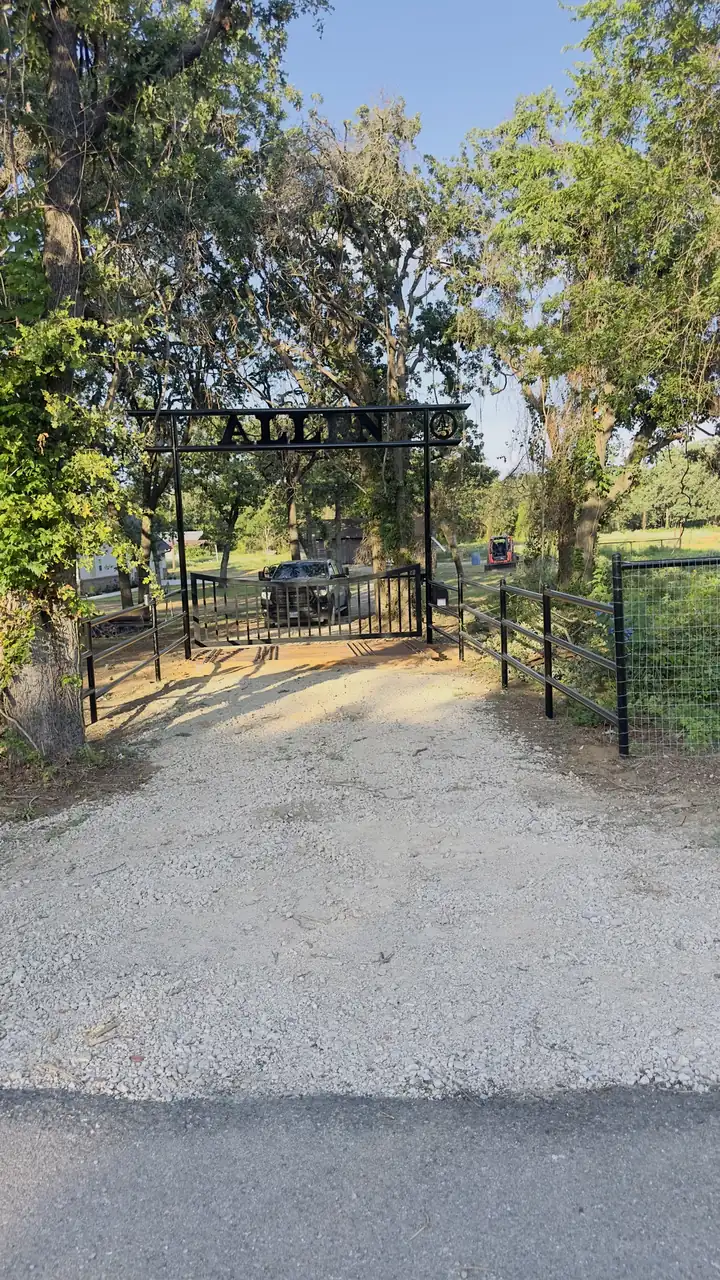 Iron arch gate on a tree-lined drive by Aesthetic Gates & Fence in Navarro County, Texas